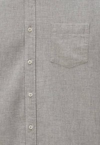 Chemise boutonnee grise claire à l'avant avec une poche poitrine sur le côté gauche, comportant quatre boutons blancs visibles.