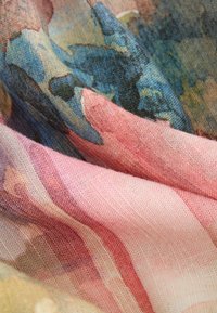 Gros plan sur un tissu replié et texturé avec un imprimé floral de style aquarelle dans des tons de rose, bleu et beige.