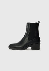 Botte cheville en cuir noir avec des panneaux latéraux élastiques, bout arrondi et talon carré. Texture lisse et détails en couture.