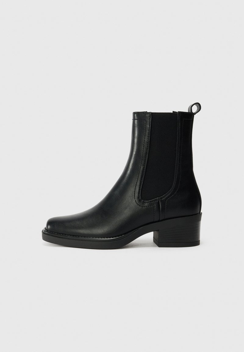Botte cheville en cuir noir avec des panneaux latéraux élastiques, bout arrondi et talon carré. Texture lisse et détails en couture.