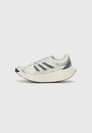 Chaussure de sport blanche et argentée avec des bandes noires, semelle épaisse et incurvée, dessus en mesh et design à lacets, vue de côté sur fond uni.