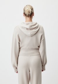 Hoodie in maglia beige chiaro con una vestibilità comoda, orlo e polsini a coste, caratterizzato da una cucitura centrale sul retro e un tessuto morbido e texturizzato.