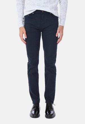 Chino blu navy slim fit in cotone, caratterizzati da una texture liscia, cinque tasche e dettagli in metallo. Abbinati a scarpe nere con lacci.
