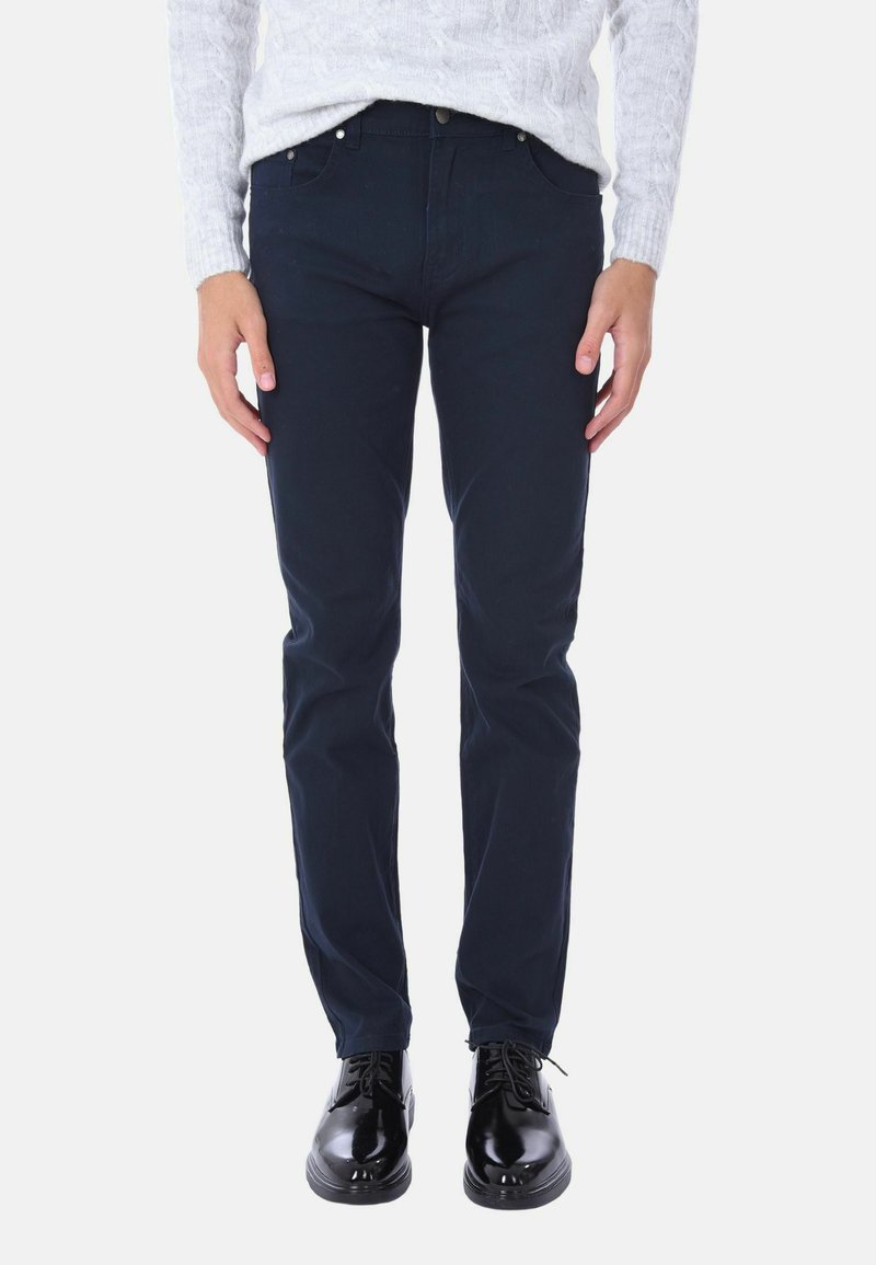 Chino blu navy slim fit in cotone, caratterizzati da una texture liscia, cinque tasche e dettagli in metallo. Abbinati a scarpe nere con lacci.
