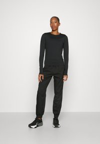 Black long-sleeve top with a round neckline, paired with relaxed-fit black track pants. Black athletic shoes with gray accents complete the outfit.