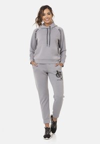 Graue Kapuze mit Logo-Akzenten, Kordeln mit Farbspitzen und passenden Jogginghosen mit Logo-Druck. Weicher Stoff, lässige Passform.