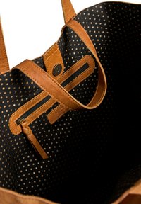 Intérieur d'un sac fourre-tout en cuir marron avec doublure en tissu noir et petits pois beiges, comportant une poche zippée et une fermeture à bouton magnétique.