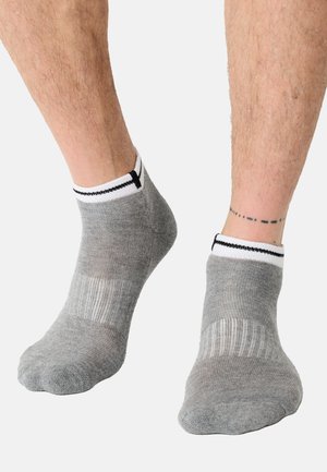 Calzini alla caviglia grigi con una texture a coste, caratterizzati da un polsino bianco e una striscia nera, che mostrano una vestibilità aderente alla caviglia.