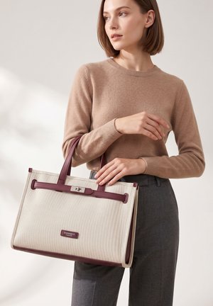 Femme portant un pull beige et un pantalon gris, tenant un sac cabas beige et bordeaux Diana&Co Firenze avec doubles anses.