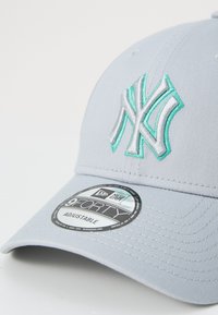 Gorra de béisbol gris con correa ajustable, que cuenta con un logotipo bordado en plata y aqua en relieve. Tejido texturizado y visera curva.