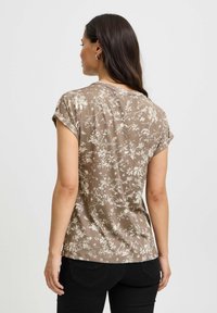 Brun blomstret bluse med korte ærmer. Lavet af letvægtsstof, har en rund halsudskæring og en afslappet pasform.