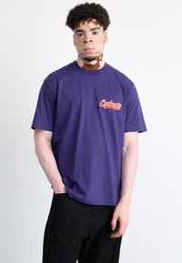 Purple cotton t-shirt featuring a rounded neckline and short sleeves, adorned with a red Carhartt logo on the left chest area.