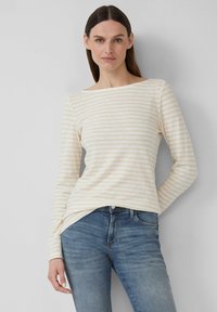 Cream long-sleeve top with light beige stripes, featuring a boat neckline. Paired with blue jeans, showcasing a relaxed fit.