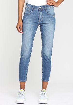 Jeans azules ajustados y recortados combinados con zapatillas blancas y amarillo neón, mostrando vista frontal desde la cintura hasta los tobillos.