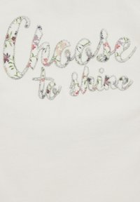 Baltas audinys, papuoštas fraze "Pasirink švytėti" gėlių raštu su blizgiais akcentais. Tekstas turi tekstūrinį, siuvinėtą išvaizdą.