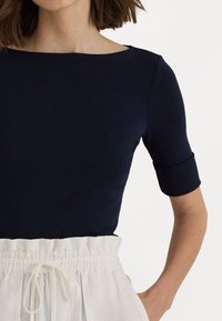 Navy blue short-sleeve top with a boat neckline and a smooth texture, paired with a cream-colored elastic waistband skirt.
