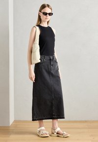Black denim maxi skirt, fitted at the waist. Black sleeveless top, light textured crossbody bag, white strappy sandals with thick straps.