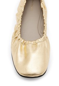 Ballerina d'oro realizzata in pelle metallica, con bordi arricciati, punta tondeggiante e suola in gomma nera per comfort e flessibilità.