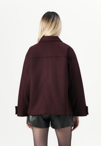 Veste d'extérieur bourgogne à coupe décontractée, avec un large col et de grands poignets. Fabriquée en mélange de laine texturé, elle présente un design à dos droit.