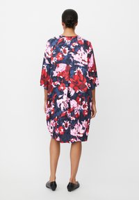 Bloemenjurk met een marineblauw, rode en roze patroon, losse pasvorm, driekwart mouwen, knie-lengte en zachte stof. Zwarte flats gedragen.