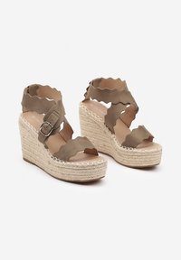 Sandales à talon compensé avec un dessus en olive vert doux et ondulé, plateforme en jute tressé et sangle de cheville à boucle. Fini texturé sur le matériau.