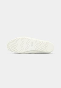 Semelle de chaussure en caoutchouc blanc présentant un motif en zigzag texturé et un logo "TOMS" en relief. Finition lisse avec des bords arrondis.