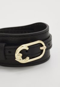 Cintura in pelle nera con una fibbia dorata. Il cinturino è liscio, con cuciture visibili e fori per la regolazione. La fibbia presenta un design distintivo a loop.