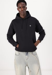 Zwarte hoodie met een kangoeroezak aan de voorkant en logo op de borst, gecombineerd met lichtblauwe verwasheden denim jeans. Katoenmengsel.