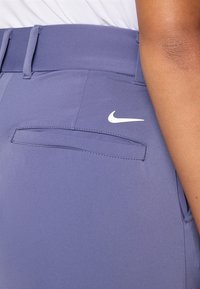 Pantalons de sport Nike en violet clair, dotés d'une texture lisse, d'une poche arrière cousue et d'un accent logo blanc.