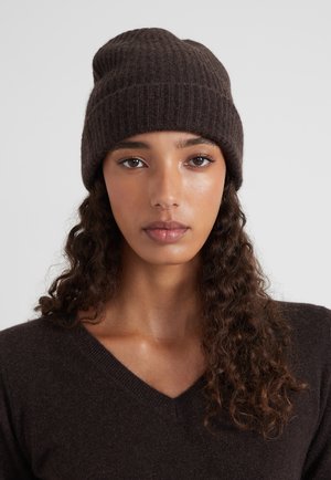 Bonnet en tricot brun avec une texture côtelée, un matériau doux et une coupe ajustée. Porté sur des cheveux ondulés mi-longs, accompagné d'un haut foncé.