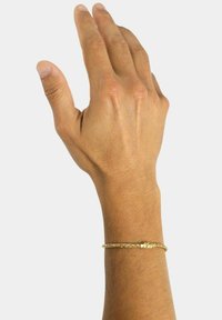 Bracciale intrecciato in oro su un polso, con chiusura a moschettone, superficie liscia e riflettente, su uno sfondo chiaro.