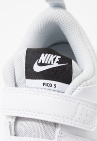 Białe skórzane sneakersy z siateczkowymi akcentami, czarna tkaninowa język z logo "NIKE" oraz etykieta "PICO 5" na białym tle. Zapięcie na rzep.