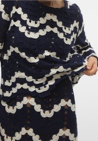 Top all'uncinetto blu navy e panna con un motivo a scallop, maniche lunghe e tessuto testurizzato, che presenta trame aperte e un design a strati.