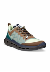 Lichtgroene en bruine sportschoen met een zwarte zool met driehoekige openingen en bruine veters met patroon, weergegeven vanuit een hoek van driekwart.