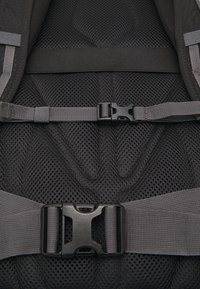 Tissu en mailles noires avec un motif texturé, présentant des sangles grises ajustables et une boucle en plastique noire pour un maintien sécurisé.