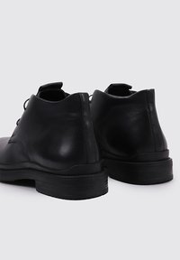 Zapatos de cuero negro con una textura suave, punta redonda y un tacón bajo y grueso. Presentan costuras mínimas y una pestaña en la parte trasera.