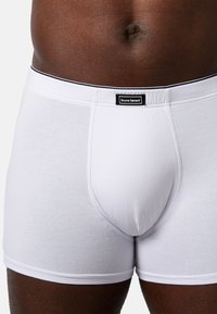 Boxer in cotone bianco con una vestibilità aderente, caratterizzati da un elastico nero in vita e un'etichetta al centro. Texture liscia e design semplice.