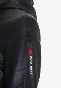 Zwarte leren jack met een capuchon, zijzak met rits en een stoffen label met "CIPO BAXX" en een rood embleem op de mouw.