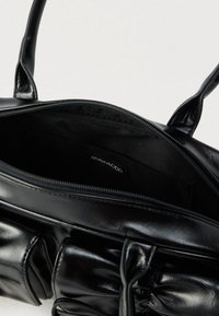 Czarna torebka syntetyczna z zamkiem błyskawicznym, miękką, puszystą teksturą i dwoma solidnymi uchwytami. Wnętrze z gładką, czarną podszewką.