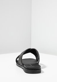 Svart platt sandal med flätade remmar, en slät lädersula och en minimalistisk design med låg profil.
