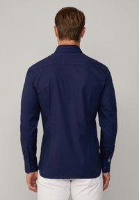 Navyblauw langslievend overhemd met een button-down kraag, met een soepele textuur en een getailleerd ontwerp, weergegeven vanuit de rug.