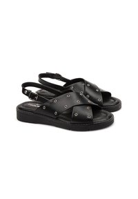 Sandalias de cuero negro con correas cruzadas que presentan acentos de ojales de metal. Suela plana con diseño de espalda ajustable y hebilla.