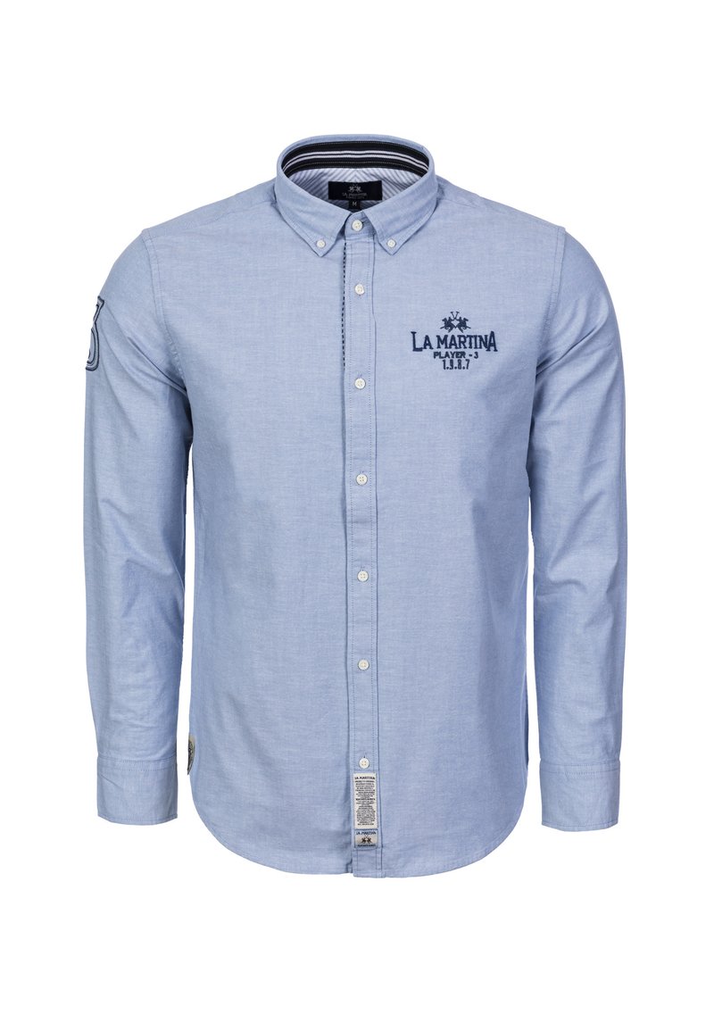 Vaaleansininen nappipaita, joka on valmistettu pehmeästä kankaasta. Siinä on pitkät hihat, kaulus, kirjailtu logo ja merkki alaosassa sivulla.