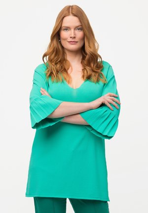 Blusa turchese con scollatura a V profonda e maniche a campana plissettate, realizzata in un tessuto morbido e leggero. Texture liscia, vestibilità ampia.