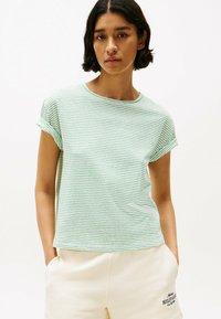 Camiseta de rayas verde claro con cuello redondo y mangas cortas dobladas. Tela suave con un corte relajado, combinada con pantalones cortos crema.