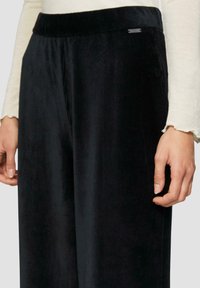 Zwarte corduroy wijde pijpen broek met een gladde tailleband en subtiele textuur. Heeft een klein label nabij de tailleband.