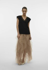Top nero con scollo a V e bordo in pizzo abbinato a una gonna in tulle traslucido color beige a strati. L'outfit presenta voluminose rouches e una silhouette fluida.