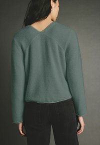 Maglione lavorato a maglia color teal con scollo a V e maniche lunghe, caratterizzato da una texture morbida e cuciture a contrasto, abbinato a jeans neri.