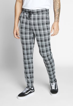 Czarno-białe spodnie w kratę o zwężanym kroju, z elastycznym paskiem z sznurkiem. Połączone z czarno-białymi sneakersami.