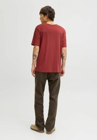 Roodbruin katoenen t-shirt met korte mouwen, ontspannen pasvorm en ronde hals, gecombineerd met olijfgroene broek en lichtgekleurde schoeisel.